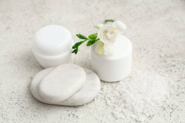 Kavanozlar dolusu kozmetik ürünler, spa taşları ve açık arkaplanda frezya çiçeği.