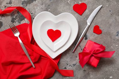 Kalp şeklinde tabaklar, peçete, hediye kutusu ve arkaplanda kağıt kalplerle Sevgililer Günü için masa ayarlayın.