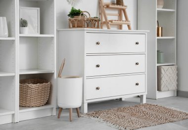 Oturma odasının içinde çekmeceler, raf üniteleri ve çöp kutusu var.