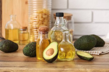 Beyaz tuğla duvarın yanındaki ahşap masada taze avokado yağı şişeleri ve sürahisi.