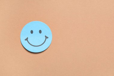 Kahverengi arka planda gülen yüzlü yapışkan bir not.