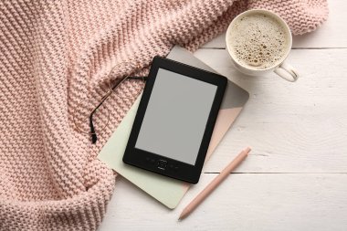 Not defteri, bir fincan kahve ve beyaz ahşap arka planda battaniyesi olan modern bir e-okuyucu.