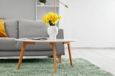 Gri kanepesi ve kahve masasında güzel narsisli çiçekleri olan şık bir oturma odası.