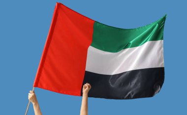 Mavi zemin üzerinde BAE bayrağı sallayan, sıkılmış yumruklu kadın elleri