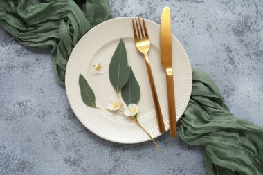 Tabak, çatal bıçak, peçete, yasemin çiçekleri ve gri grunge arkaplanlı yapraklarla süslü masa.