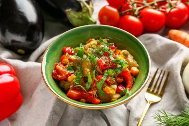 Bir kase sebze yahnisi, domates, patlıcan, havuç ve peçetede otlar.