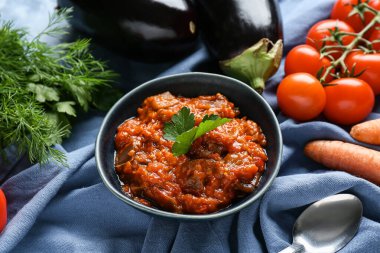 Bir kase sebze yahnisi, patlıcan, domates ve mavi peçeteli otlar.