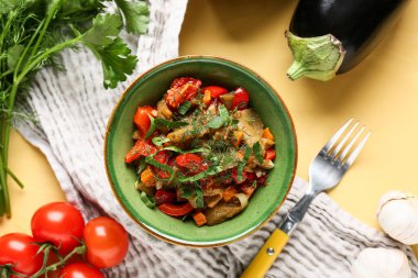 Bir kase sebze yahnisi, domates, patlıcan, havuç ve sarı arka planda otlar.