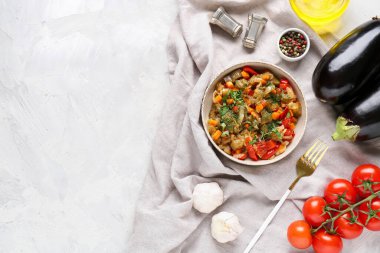 Bir kase sebze yahnisi, domates, patlıcan, havuç ve hafif arka planda bitkiler.