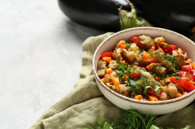 Bir kase sebze yahnisi, domates, patlıcan, havuç ve hafif arka planda bitkiler.