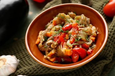 Bowl of vegetable stew with tomatoes, eggplant, carrots and herbs on green napkin