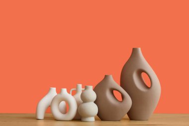 Turuncu duvara karşı ahşap masada bir sürü farklı vazo var.