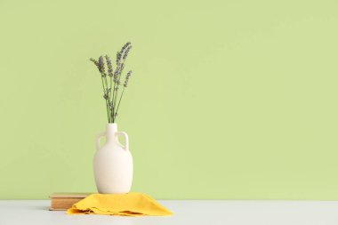 Lavanta çiçekli vazo, yeşil duvara karşı beyaz masada kitap ve peçete.