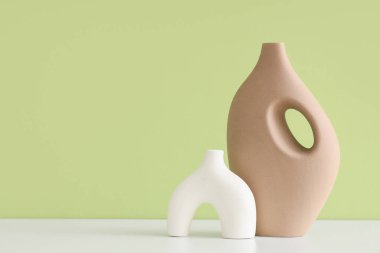 Yeşil duvara karşı beyaz masalarda farklı vazolar.