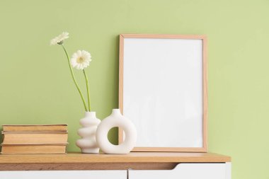 Farklı vazolarda papatya çiçekleri, kitaplar ve klozetin üzerindeki yeşil duvarlar.