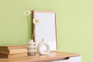 Farklı vazolarda papatya çiçekleri, kitaplar ve klozetin üzerindeki yeşil duvarlar.