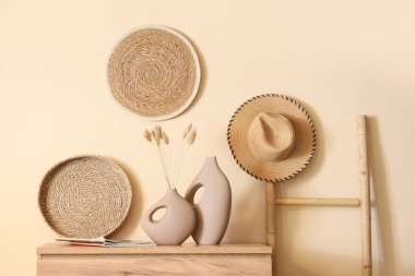 İçinde laguru, dergi ve hasır tepsi olan vazolar bej duvarın yanındaki ahşap klozette.