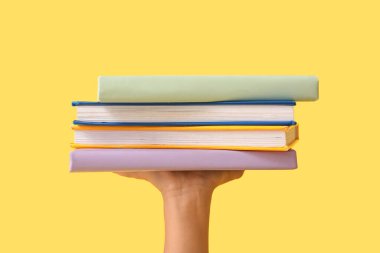 Sarı arka planda renkli kitaplarla dolu bir çocuk eli