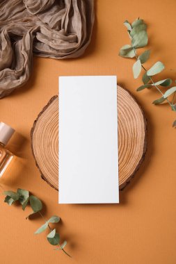 Tahta tahta tahta, boş kart, okaliptüs dalları ve turuncu arka planda kumaş.