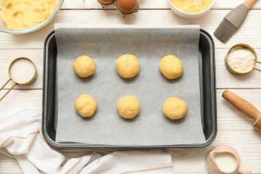 Pişmemiş kurabiyeler ve beyaz ahşap arka planda malzemelerle pişirme tabağı.