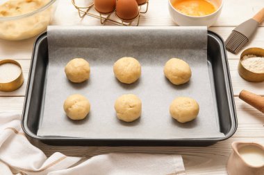 Pişmemiş kurabiyeler ve beyaz ahşap arka planda malzemelerle pişirme tabağı.