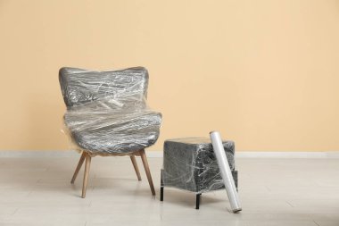 Sarılı gri kanepe ve bej duvarın yanında gerilmiş film rulosu ile puf.