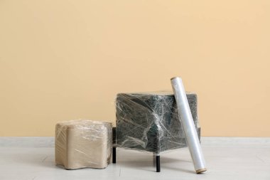 Bej duvarın yanında streç film rulosu olan paketlenmiş puflar