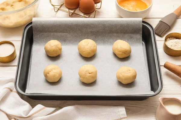 Pişmemiş kurabiyeler ve beyaz ahşap arka planda malzemelerle pişirme tabağı.