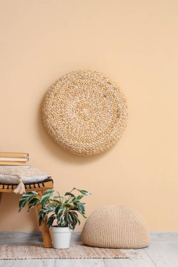 Yumuşak örülmüş pouf çiçekli ve bej duvarın yanında ahşap tabure var.