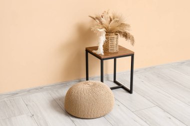 Bej duvarın yanında yumuşak örülmüş puf ve şık bir masa.