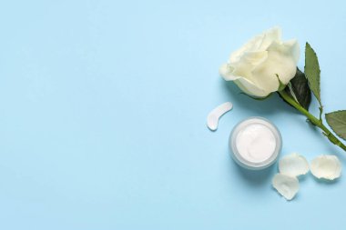 Yapraklı güzel beyaz gül çiçeği ve mavi arka planda kozmetik krem kavanozu