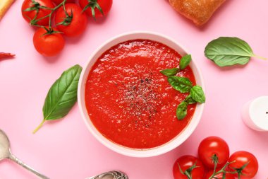 Bir kase lezzetli domates çorbası ve pembe arka planda malzemelerle yakın plan kompozisyonu.