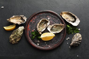 Lezzetli taze istiridye, limon ve maydanozlu siyah arka plan.