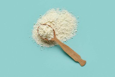 Tahta kaşık, turkuaz arka planda süt tozu.
