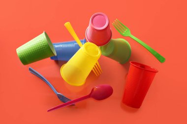 Renkli plastik bardaklar ve çatal bıçak takımı kırmızı zeminde uçuyor.