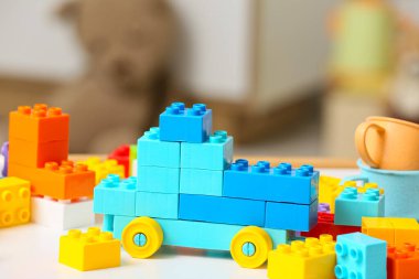 Çocuk odasındaki beyaz masanın üzerindeki renkli plastik yapı taşlarından yapılmış oyuncak araba.