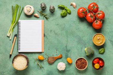 Boş tarif kitabından yapılmış çerçeve, baharatlar, otlar ve yeşil grunge arka planda taze sebzeler