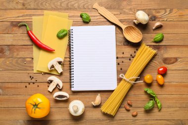 Boş tarif kitabıyla kompozisyon, çiğ makarna ve ahşap arka planda taze sebzeler.