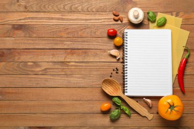 Boş tarif kitabıyla kompozisyon, çiğ makarna ve ahşap arka planda taze sebzeler.
