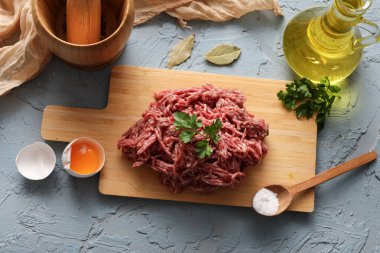 Tahta tahtada taze et, maydanoz, kırık yumurta ve mavi grunge arka planda bir sürahi yağ var.