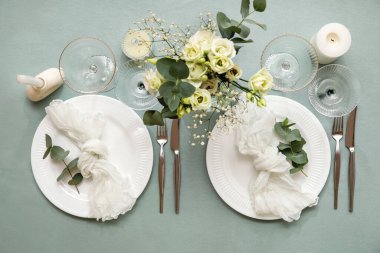 Gri masa üzerinde peçeteler, okaliptüs dalları, bardaklar ve çiçekler olan güzel bir düğün masası.