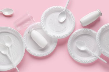 Plastik tabaklar, fincanlar, şişeler ve pembe arka planda çatal bıçak.