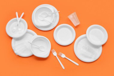 Turuncu arka planda farklı plastik sofra takımı ve çatal bıçak takımı
