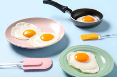 Tabak ve tavada mavi arka planda leziz yumurta, yakın plan.