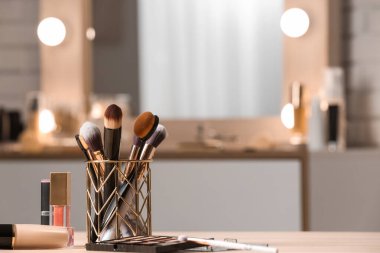 Ahşap masadaki fırçalı farklı makyaj ürünleri bulanık arka planda