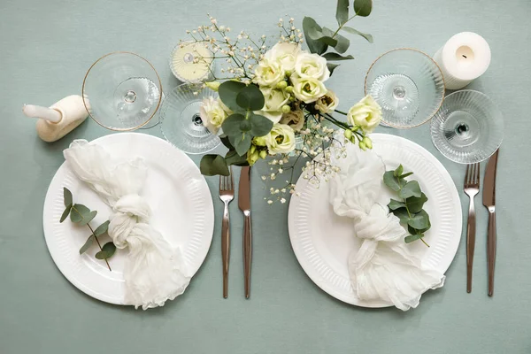 Gri masa üzerinde peçeteler, okaliptüs dalları, bardaklar ve çiçekler olan güzel bir düğün masası.