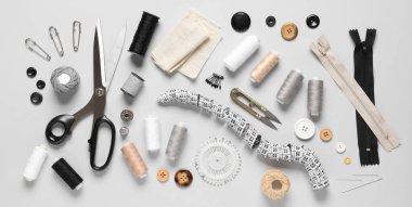 Kumaşlı iplik makaraları, ölçüm bandı, makas ve gri arkaplanda dikiş malzemeleri