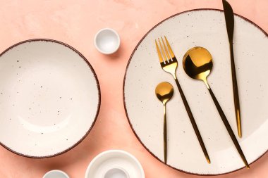 Temiz tabak, kase ve pembe masadaki altın çatal bıçak takımı.