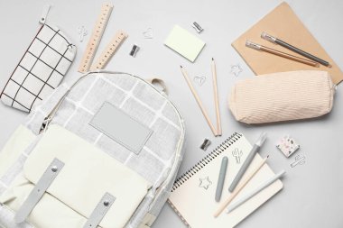 Gri arka planda farklı kırtasiye malzemeleriyle süslü okul çantası.