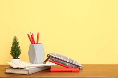 Farklı kırtasiye malzemesi, ev bitkisi ve ahşap masadaki not defterleri olan tutucu.